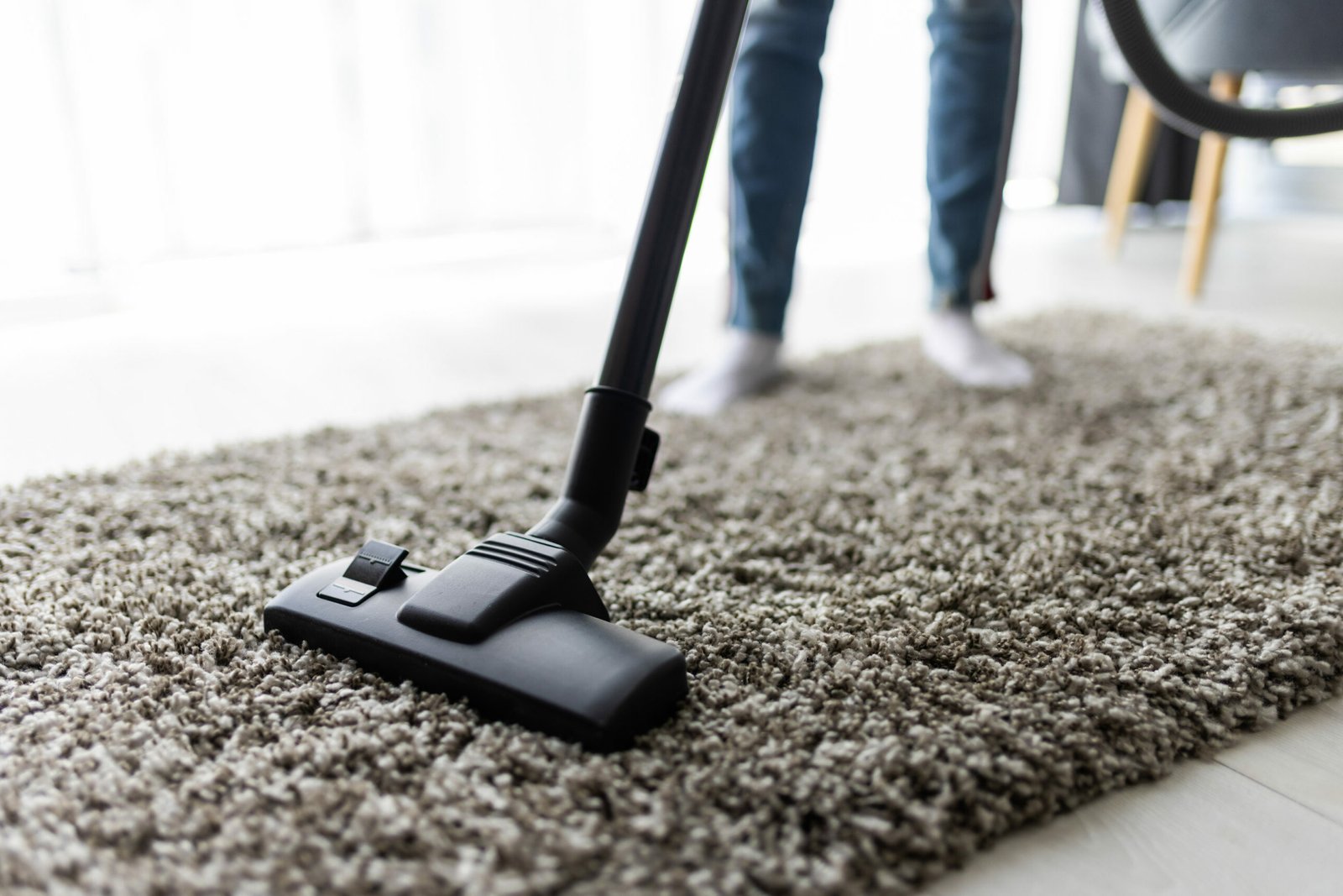 Close up of woman with legs vacuum cleaner cleaning carpet at home