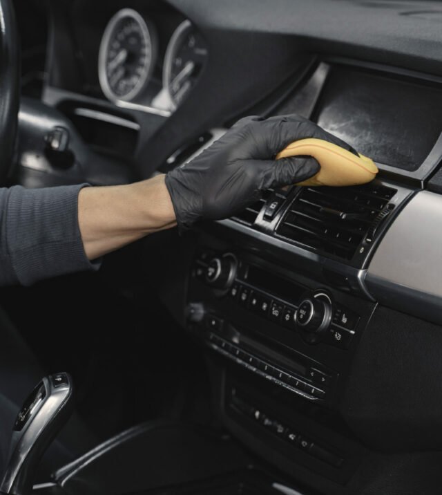 Man in a garage. Worker polish inside a car. Man in a black uniform.